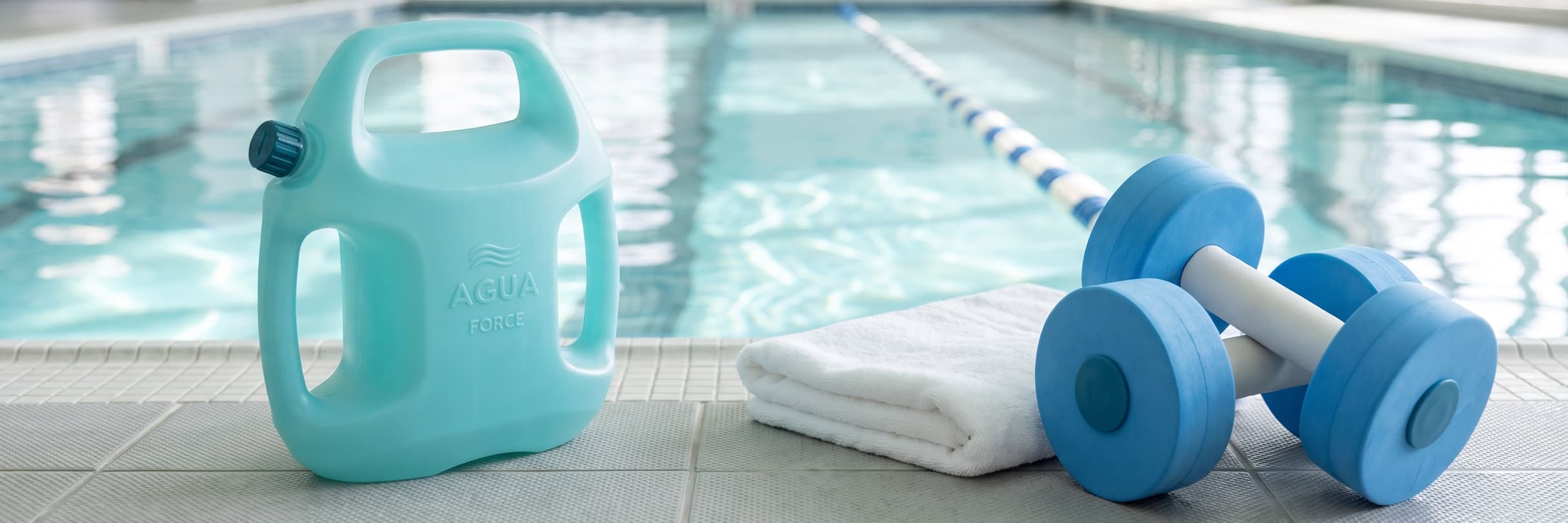 An aqua AguaForce water-filled weight, a folded white towel and a pair of blue foam aqua dumbbells on the deck of a bright indoor pool